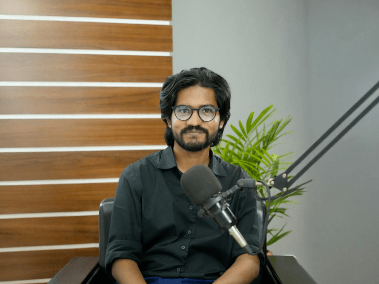 A confident South Asian man in a studio, ready for podcasting with a professional microphone setup.
